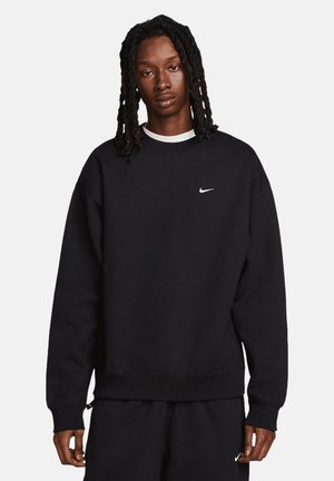 Czarny dres Nike z okrągłym dekoltem, długimi rękawami i logo na piersi. Materiał wydaje się miękki, z ściągaczami przy rękawach i dole.
