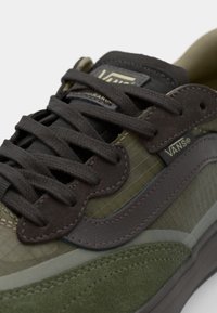 Olive green Vans sneakers with textured suede and synthetic materials, featuring dark brown laces, a logo tag, and a contrasting side stripe.