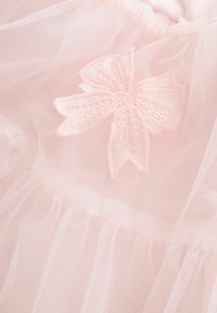 Delikāta rozā caurspīdīga auduma ar volānu slāņiem un izšuvuma detaļu tauriņš ar saskaņotu rozā diegu.