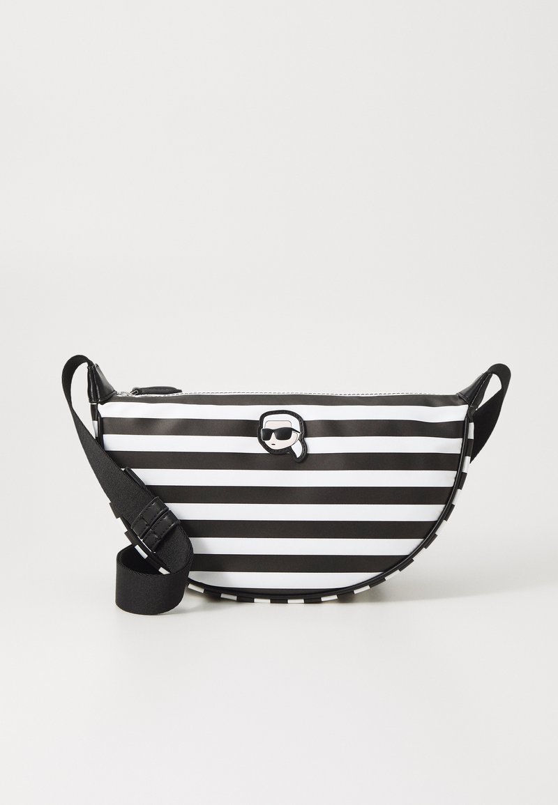 Bolso bandolera de rayas en blanco y negro con cierre de cremallera, forma redondeada, correa desmontable y un pequeño acento de logo circular.