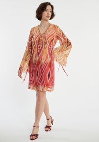 V-Ausschnitt, langärmeliges Kleid in lebhaften Rot-, Orange- und Gelbtönen. Leichtes, semi-transparentes Material mit ausgestellten Ärmeln und Kordelzugdetails.