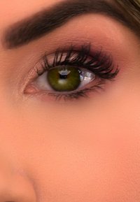 Nahaufnahme eines Auges mit grüner Iris, dunklen Wimpern, dezentem rosa Lidschatten und sanft strukturierter Haut drumherum. Definierte Augenbraue über dem Auge.