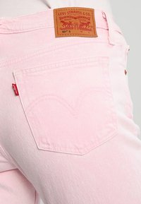 Jeans de mezclilla rosa claro con un parche de cuero distintivo que incluye la marca, cinco bolsillos y un patrón de costura distintivo en la parte posterior.