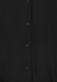 Schwarzes Kleidungsstück mit flachen schwarzen Knöpfen und einer strukturierten Oberfläche. Enthält eine geraffte Taillendetailung und glatten Stoff.