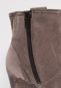 Gray suede ankle boot featuring a side zipper, stitched accents, and a wooden heel with decorative metal studs.