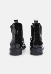 Botas Chelsea de charol negro con paneles laterales elásticos, tiradores y suelas de goma gruesa, con una textura lisa y brillante.