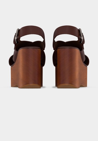 Sandales compensées en cuir marron avec larges talons blocs en bois et brides réglables à la cheville, vues de dos sur un fond blanc.