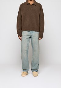 Brun stickad polo-tröja, ljusblå slitna jeans, krämfärgade slip-on skor med sömdetaljer, bärs tillsammans som en outfit.