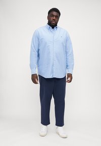 Lichtblauwe button-up shirt van katoen, gecombineerd met marineblauwe broek, gedragen met witte sneakers. Soepele textuur en ontspannen pasvorm.