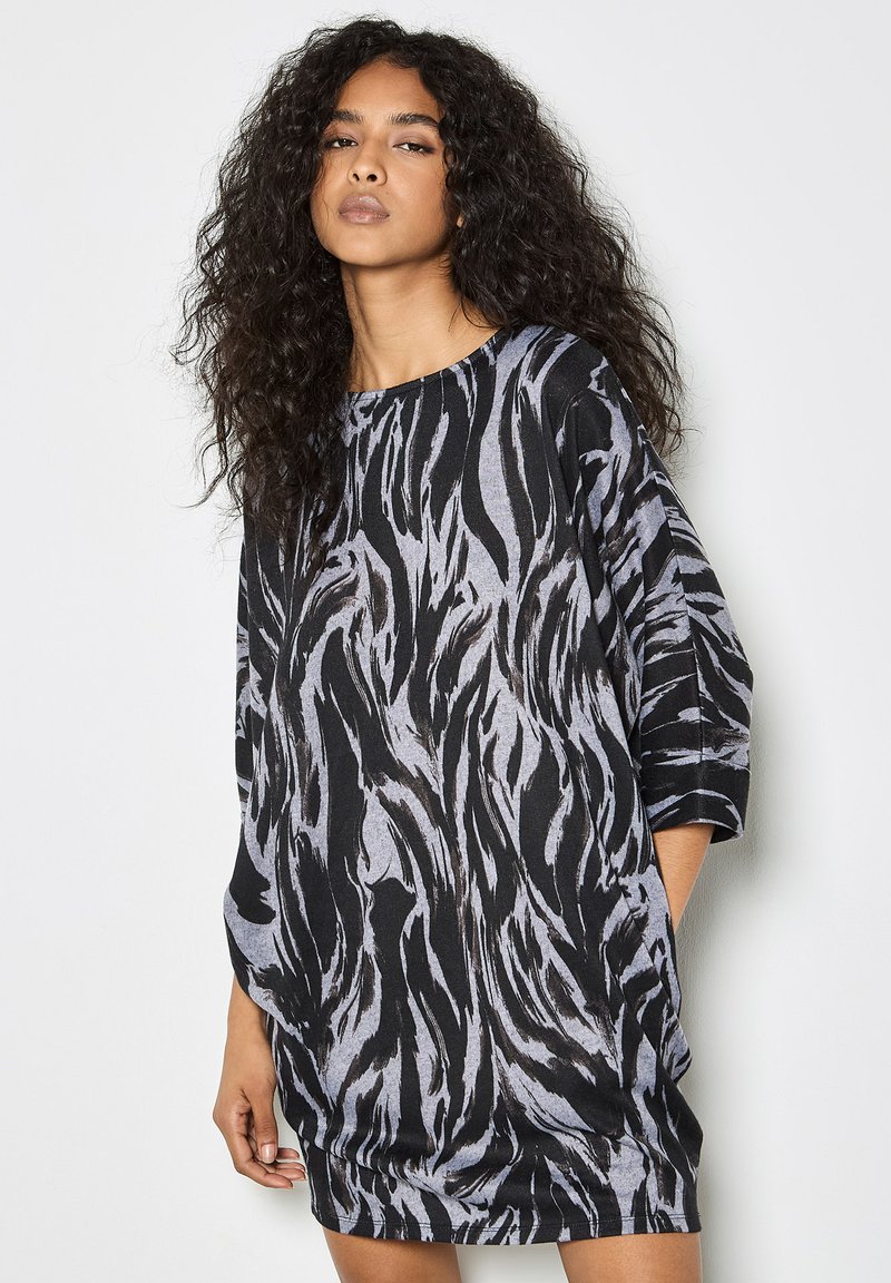 Schwarzes und graues, übergroßes Kleid mit einem wirbelnden Muster, dreiviertelärmlig und mit Rundhalsausschnitt, aus einem weichen Stoff gefertigt.