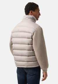 Polstret jakke i lys beige og blød grå. Krave, ribstrikkede manchetter. Lodret quiltet mønster på forsiden, glat stof på ærmerne. Casual design.