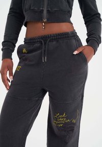 Svarta joggers i bomullsblandning med elastisk midja, sidofickor, broderad gul text och grafiska detaljer på benen.