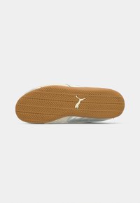 Semelle d'une basket avec une semelle en caoutchouc brun texturée et un logo Puma blanc au centre, sur un fond gris clair.