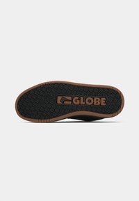 Fekete gumi talp, texturált tapadással és barna részletekkel, a "GLOBE" logó bemélyesztve. Rugalmas, áramvonalas kialakítású lábbeli.