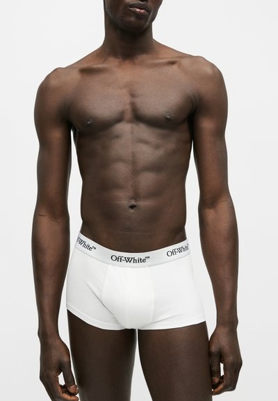 Άνδρας με λευκά μπόξερ Off-White, σε απλό ανοιχτό γκρι φόντο.