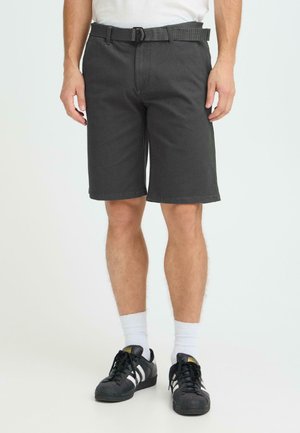 Mann trägt dunkelgraue knielange Shorts mit schwarzem Gürtel, weiße Socken und schwarze Adidas-Sneaker mit weißen Streifen.