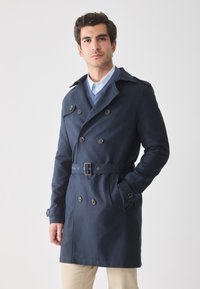 Gabardina azul marino con botones de doble botonadura, amplio cuello, cintura ceñida con cinturón y bolsillos laterales. Fabricada con un tejido suave de peso medio.