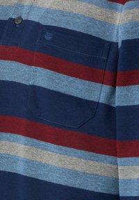 Ubranie w paski w kolorze granatowym, czerwonym i jasnoniebieskim. Posiada kieszeń zapinaną na guzik, teksturowany materiał oraz zaokrąglony dół. Pionowe paski rozmieszczone w odstępach.