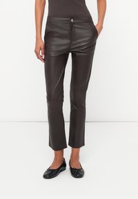 Pantaloni din piele maro, cu o croială slim, având închidere cu nasture, buzunare laterale și o textură netedă. Asortați cu balerini negri.
