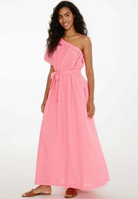 Ružová, jednoramenná maxi šaty so zúženým pásom a detailom na viazanie. Neformálny, ľahký materiál s voľným strihom. Nosené ploché sandále.