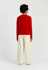 Roter Pullover mit langen Ärmeln, kombiniert mit cremefarbenen, weiten Hosen. Weiche Textur, minimalistisches Design und gerader Schnitt.