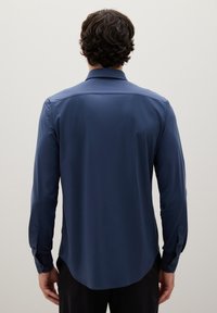 Camicia a maniche lunghe blu navy con orlo curvo, texture liscia, colletto classico e polsini con bottoni, che presenta un design minimalista.
