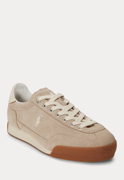 Baskets décontractées en daim beige avec lacets blancs, logo blanc sur le côté et semelle en caoutchouc marron.