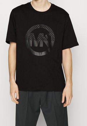 Czarna bawełniana koszulka z krótkim rękawem, z dużym, półprzezroczystym okrągłym logo z literami "MK" na środku. Luźny krój.