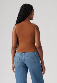 Brun uten ermer topp med et figursydd design, kombinert med høytlivte blå jeans med klassisk fem-lommers design og synlig søm.