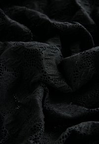 Tissu en dentelle noire avec un motif texturé présentant des designs floraux et des mailles ouvertes, froissé pour créer des plis doux.