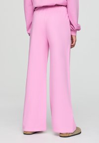Pantaloni della tuta rosa a gamba larga realizzati in materiale morbido con cintura elastica; texture liscia e senza motivi o accenti visibili.