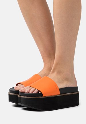 Plattformssandaler med en orange gummiyta och en svart texturerad sula. Designen har ett brett rem och en tjock bas som framhäver kontrasten.