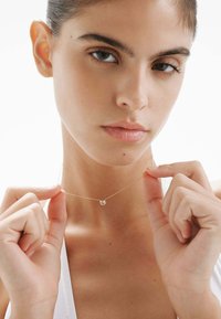 Collar de cadena de oro con un pequeño colgante redondo, exhibido sobre un fondo claro. Presenta eslabones finos y un detalle brillante en el colgante.