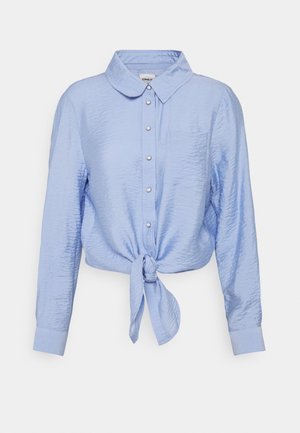 Camicia azzurro chiaro con colletto, maniche lunghe e un nodo sul davanti. Tessuto strutturato con patta dei bottoni e una singola tasca sul petto.