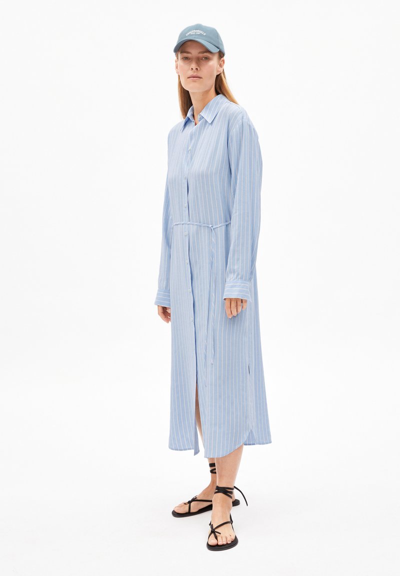 Robe longue à rayures bleu et blanc avec un devant boutonné, un col et des manches longues ; associée à des sandales plates noires à lanières.