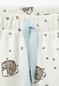 Pantalones cortos de tela blanca con un patrón de perezosos sobre nubes, acentos de estrellas y un cordón azul claro en la cintura.