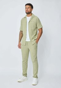 Chemise à manches courtes vert clair et pantalon assorti en tissu texturé, associés à un t-shirt blanc et des sneakers blanches.