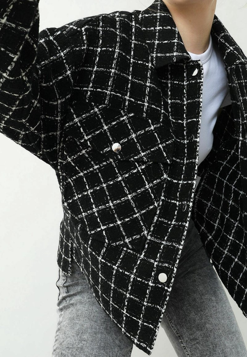 Svartvit rutmönstrad jacka med strukturerat tyg, med krage, framfickor och silverfärgade tryckknappar.