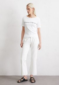 Hvid kortærmet t-shirt med "Marc O'Polo" tekst. Kombineret med hvide flagrende bukser og sorte slidesandaler med en guldspænde detalje.