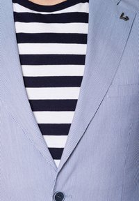 Błękitny żakiet w paski z klapami, w połączeniu z marynarską koszulą w biało-niebieskie paski. Posiada zapięcie na guziki i subtelny detal z logo.