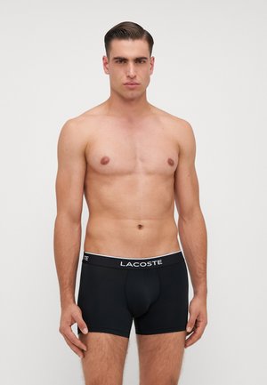 Boxer da uomo in cotone nero con cintura bianca con logo Lacoste. Il design presenta una vestibilità aderente e una texture liscia. Nessun ulteriore motivo o accento.