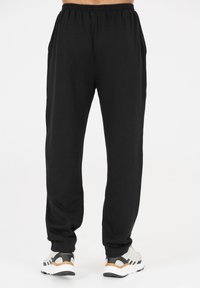 Zwarte sweatpants van zachte stof, met een elastische tailleband, zijzakken en een taps toelopend ontwerp. Gecombineerd met witte sneakers.