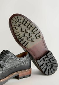 Black leather shoes with textured design, wingtip detailing, and a wooden heel. Rubber sole features a rugged tread pattern for grip.