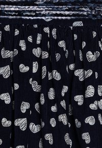 Námořnická modrá látka s ribovanou strukturou, s celoplošným bílým vzorem srdcí různých velikostí a s nařasením na lemu.