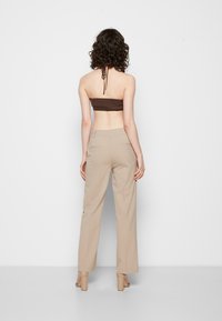 Top castanho sem alças combinado com calças largas bege e sapatos de salto bege. O top possui um design texturizado e um detalhe de laço nas costas.