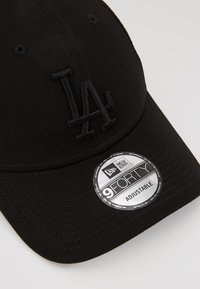 Căciulă de baseball neagră cu logo brodat "LA", design ajustabil 9FORTY, textură de material neted și vizor curbat. Include autocolant argintiu New Era.