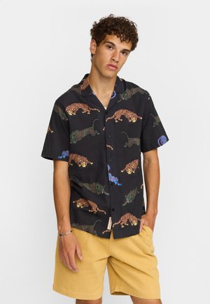 Zwart T-shirt met korte mouwen en kleurrijke luipaardpatronen, gemaakt van lichtgewicht stof. Gecombineerd met beige korte broek.