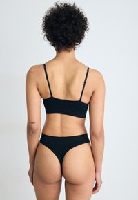 Mustalainen ribbiohenteinen bralette ja korkeavyötäröinen bikinit setti. Sisältää säädettävät hihnat ja saumattomat reunat sujuvaa istuvuutta varten, esittäen minimalistista muotoilua.