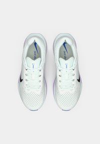 Baskets blanches avec une tige en mesh, logo Nike noir et semelle extérieure violette. Elles présentent un système de laçage et la phrase "just do it" sur la semelle intérieure.