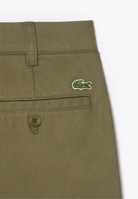 Olijfgroene katoenen broek met een klein geborduurd krokodillenlogo, een knoopsluiting en details op de achterzak.